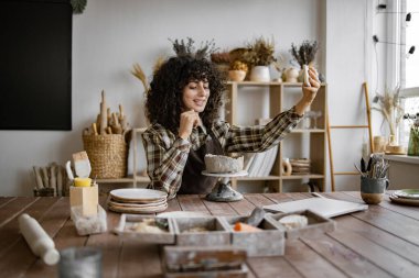 Kadın çömlekçi, rahat ve iyi ışıklandırılmış bir çömlek stüdyosunda kilden bir heykel üzerinde çalışırken bir video kaydediyor..