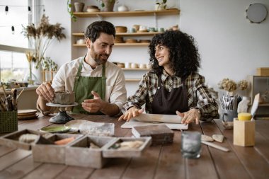 Önlüklü sakallı olgun bir adam vazo yontuyor. Bir kadın ise çömlek atölyesinde merdaneyle kil yuvarlıyor..
