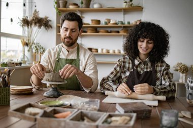 Çömlek atölyesinde kilden heykel yapan olgun bir adam ve kadın. Erkek vazoyu şekillendirir, kadın da merdaneyle toprağı yuvarlar..