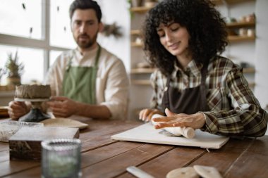 Sakallı olgun bir adam vazo yontuyor ve genç bir kadın çömlekçilik sınıfında oklavayla yuvarlanıyor..