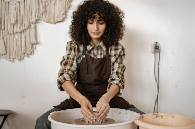 Stüdyoda çömlekçi çarkını kullanarak seramik bir çanak heykel yapan kadın. Çömlek yapımında odaklanma ve yaratıcılık.