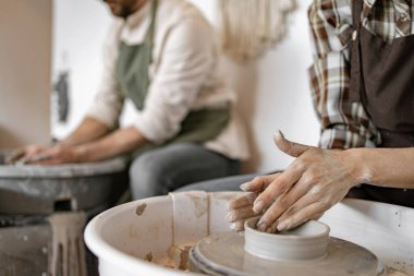 Kadın ve erkek çömlekçi çarkında birlikte çalışarak kil çömlek yapıyorlar. Sanat stüdyosunda kil vazo şekillendiren eller. Yaratıcılık, işçilik ve takım çalışması..