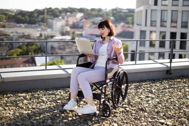 Tekerlekli sandalyedeki genç ve güzel kadın iş görüşmesi sırasında görüntülü konuşma yapıyor. Çevrimiçi uzaktan kumanda ve engellilik kavramı.