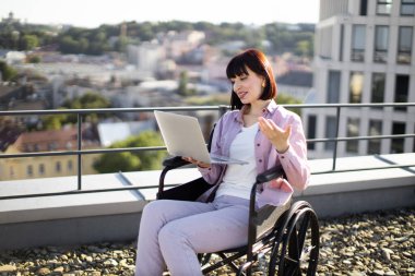 Tekerlekli sandalyedeki genç ve güzel kadın iş görüşmesi sırasında görüntülü konuşma yapıyor. Çevrimiçi uzaktan kumanda ve engellilik kavramı.
