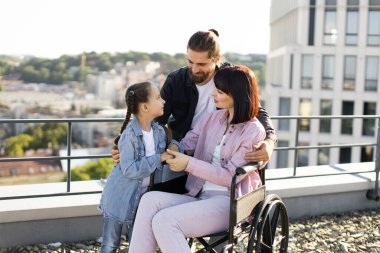 Baba ve kızı, boş zamanlarını temiz havada geçirirken anneyi ciddi yaralanma tedavisinde destekliyor. Tekerlekli sandalyedeki genç kadın modern evin terasında ailesiyle eğleniyor..