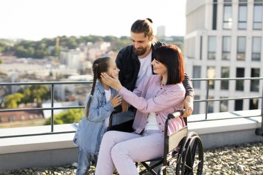 Baba ve kızı, boş zamanlarını temiz havada geçirirken anneyi ciddi yaralanma tedavisinde destekliyor. Tekerlekli sandalyedeki genç kadın modern evin terasında ailesiyle eğleniyor..