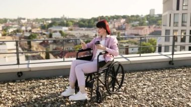 Tekerlekli sandalyedeki kadın kahveden zevk alıyor ve çatıda şehir manzaralı bir akıllı telefon kullanıyor. Rahat ve memnun görünüyor, ulaşılabilirliği ve modern yaşam tarzını kucaklıyor..