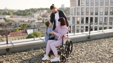 Tekerlekli sandalyedeki genç kadın modern evin terasında ailesiyle eğleniyor. Baba ve kızı, anneye ciddi yaralanma tedavisinde destek olurken boş zamanlarını temiz havada geçiriyorlar..