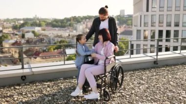 Özürlü genç bir ailenin portresi modern evlerle şehir planına karşı. Genç bir adam ve küçük bir kız tekerlekli sandalyede tedavi gören anneyle ilgileniyorlar..