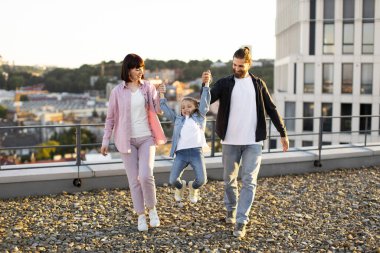 Neşeli aile çatıda kaliteli zaman geçiriyor. Ebeveynler yürürken çocuklarının ellerini tutarlar. Mutlu anlar ve aile bağları.