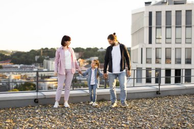 Üç kişilik bir aile, anne, baba ve çocuk, çatıda duruyorlar. Gün batımında şehir binaları ile şehir arkaplanı.