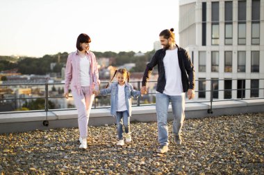 Mutlu aile çatıda eğleniyor. Anne, baba ve çocuk el ele tutuşarak birlikte yürüyorlar. Şehir manzarası.