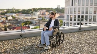 Çatıya bakan terasta tekerlekli sandalyede oturan genç adam. Kapsayıcılık, bağımsızlık ve kentsel yaşam kavramı. Gün ışığında dışarıda..