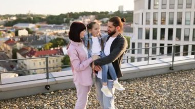 Kızlarıyla birlikte gülen ebeveynler şehir ortamında poz veriyorlar. Aydınlık bir günde aile bağı ve mutluluk.