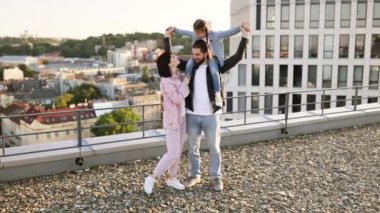 Kızı olan sevecen bir aile çatıda neşeli anlar geçirir. Arka planda güzel bir şehir manzarası vardır..