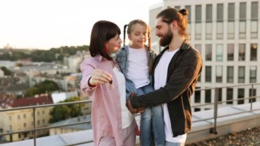 Mutlu aile çatıda duruyor, anahtarlarını tutuyor ve yeni evi genç kızıyla birlikte kutluyor, heyecan ve birlikteliği temsil ediyor..
