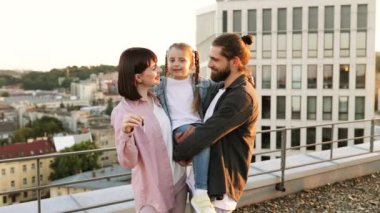 Mutlu aile şehir merkezindeki terasta yeni ev anahtarını kutluyor. Çocuklu gülümseyen ebeveynler önemli bir olayın tadını çıkarıyorlar..