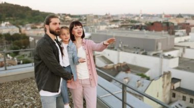 Sıcak ve neşeli bir an. Mutlu bir aile çatıda duruyor ve şehir manzarasının tadını çıkarıyor. Erkek çocuğu tutar, kadın işaret eder..