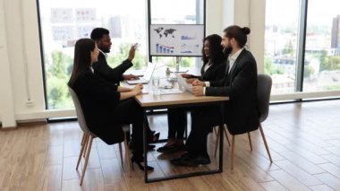 İş ekibi bir ofis toplantısı sırasında beşlik çakarak başarıyla kutluyor. Şehir görünümlü modern ofis ortamında takım çalışması, işbirliği ve başarı.