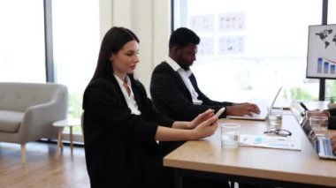 Modern ofiste iki iş adamı, akıllı telefon kullanan bir kadın, dizüstü bilgisayarda çalışan bir adam, işyerinde verimlilik, odaklanma ve teknoloji gösteren bir adam..