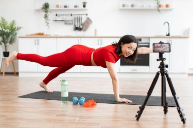 Kadın, ev mutfağında yoga dersi çekerken tahta pozu veriyor. Egzersiz ekipmanları yakında. Sağlıklı yaşam tarzını, ev çalışmasını, fitness 'i teşvik etmek..