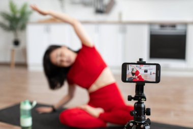 Kırmızı giysili bir kadın akıllı telefonuyla yoga seansı yapıyor. Esneme egzersizlerini telefon ekranına odaklan. Ev ödevi, spor programı ve online yoga dersi..