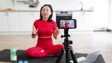Yoga dersi veren bir kadın yoga minderinde kollarını esnetiyor. Modern, parlak bir mutfakta akıllı telefonla çekim yapmak. Spor anlayışı, online öğretim ve sağlıklı yaşam tarzı..