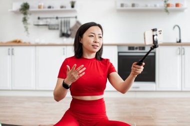 Mutfakta oturup telefon eğitimi alan bir kadın çevrimiçi blog kaydediyor. Video yaratmak için selfie çubuğu kullanırken konuşmak ve el kol hareketi yapmak. Bilgilendirici ve eğitici içerik.
