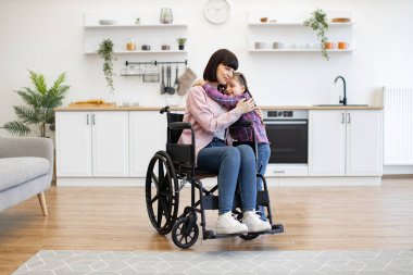 Parlak ve modern mutfak, bitkiler ve şık dekorlarla. Modern mutfakta tekerlekli sandalyeli bir anne kızına sarılıyor. Sahne sevgi, destek ve aile bağlarıyla dolu..