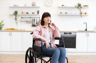 Tekerlekli sandalyedeki kendine güvenen kadın aydınlık mutfakta eğleniyor. Modern dekorlu ve pozitif titreşimli ev ortamı.