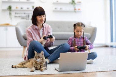 Aile bağları ve eğlence aktiviteleriyle sıcak bir ev ortamı. Anne ve kızı evcil kedileriyle oturma odasında oturmuş video oyunu oynuyorlar..