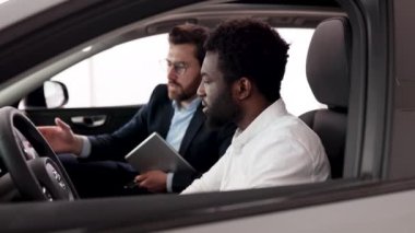 Beyaz araba satıcısı Afrikalı Amerikalı bir alıcıyla arabada oturuyor. İkisi de araba alırken gülümsüyor. Modern arabanın içinde..