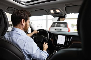 İşadamı, galeride test sürüşü yaparken arabada oturur ve yeni araba özellikleri yaşar. Direksiyon kontrol paneli.