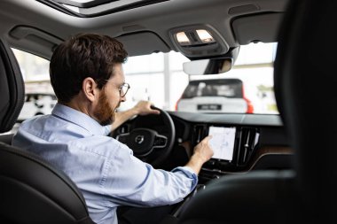 Profesyonel, parlak sergi salonunda satın alınmaya hazırlanan araba özelliklerini araştırıyor. İşadamı, galeride aracın içinde oturan dokunmatik ekranla etkileşime geçiyor..