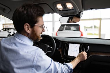 Profesyonel ortam, kullanıcı deneyimi ve yenilikçiliğe odaklanarak otomobillerdeki modern teknolojiyi gösteriyor. İşadamı aracın içinde oturuyor, araba navigasyon sistemiyle etkileşimde..