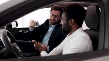 Araba özelliklerini, seçenekleri ve detayları dostça konuşarak tartışmak. Beyaz araba satıcısı Afrikalı Amerikalı bir alıcıyla arabada oturuyor..