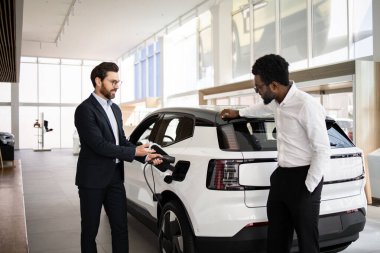 Satıcı, araba galerisindeki iş adamlarına elektrikli cip satıyor. Araç özelliklerini tartışıyorlar. İş ortamı ve modern elektrikli araç kavramı.