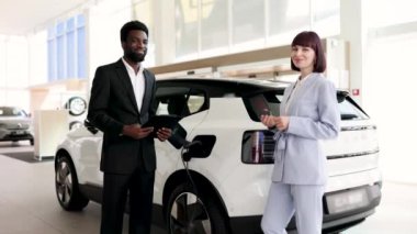 Araba galerisindeki iş kadınına elektrikli cip satan bir satıcı. İş alışverişi, sürdürülebilir ulaşım ve profesyonel toplantı. Çevre dostu araçlar için modern otomobil galerisi.