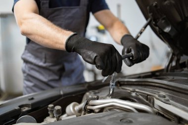 Garajdaki aletleri kullanarak araba motoru üzerinde çalışan eldiven takan tamirci elleri yakın çekimde. Bakım, onarım ve profesyonel otomotiv hizmeti kavramı.