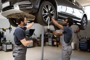 Modern garajda araç bakımında işbirliği yapan iki araba tamircisi. Profesyoneller arabaların işlevselliğini ve güvenliğini sağlamak için araç kullanıyorlar. Otomotiv servisi ve takım çalışması.