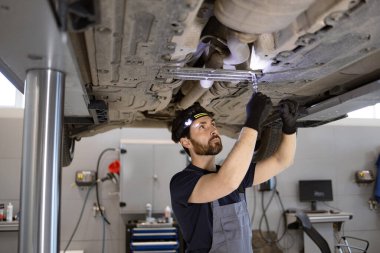 Tamirci, araba tamirhanesinde eldiven ve far takarak araç tamir ediyor. Bakım ve onarıma odaklan. Profesyonel teknisyen çalışıyor.