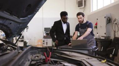 Tamirci ve işadamı atölyedeki arabayı inceliyor. Araba bakımı, araç tamiri, profesyonel danışma, müşteri hizmetleri ve teknik uzmanlık.