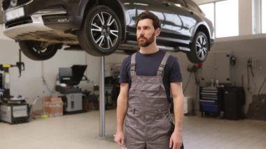 Gülümseyen tamirci asansörlü modern oto tamirhanesinde ingiliz anahtarı tutuyor. Temiz atölye ortamında araç bakım ve onarım hizmetleri için üniformalı güvenilir bir profesyonel hazır..