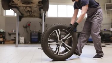 Profesyonel oto tamirhanesinde tamirci araba lastiği değiştiriyor. Tamir ve onarım için lastik taşıyan üniformalı bir işçi. Otomotiv hizmeti kavramı garaj ortamında kaydedildi.