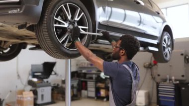 Modern otomotiv tamirhanesinde bakım için çalınan araba üzerinde çalışan tamirci. Bakım araçları ve ekipmanlar temiz ve düzenli çalışma alanlarında görünür.