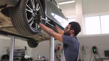 Modern oto tamirhanesinde araba tekerleği tamir eden eldiven giyen tamirci. Tamirci bakım için araç kullanırken hidrolik asansörde kaldırılan araba. Profesyonel hizmet aracı bakım ve onarım işi.