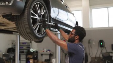 Modern garajda araba tekerleğini tamir etmek için ingiliz anahtarı kullanan gülen bir tamirci. Araç bakımında çalışan profesyonel bir teknisyen. Gözlüklü yakışıklı genç adam otomobil tamiri yapıyor..