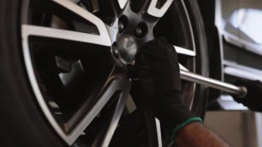 Tamirci oto tamirhanesinde araba tekerleği üzerinde çalışmak için araç kullanıyor. Teknisyen, tekerlek cıvataları sıkıyor. Modern garajda profesyonel araba bakımı ve hizmeti