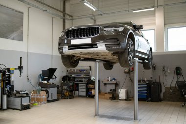 Profesyonel oto tamirhanesinde araç gereçlerle birlikte hidrolik asansörde yükseltilmiş. Araç bakımı ve denetimi için modern atölye ortamı.