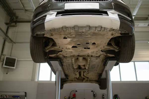 stock image Underside view of car lifted on hydraulic lift in auto repair shop for maintenance and inspection. Vehicle in garage setting ready for service.